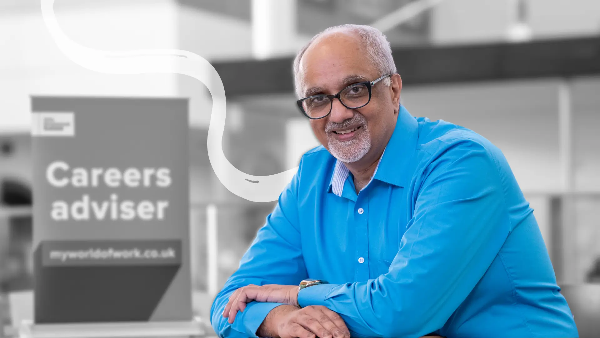 Smiling man in office next to sign reading 'Careers adviser'